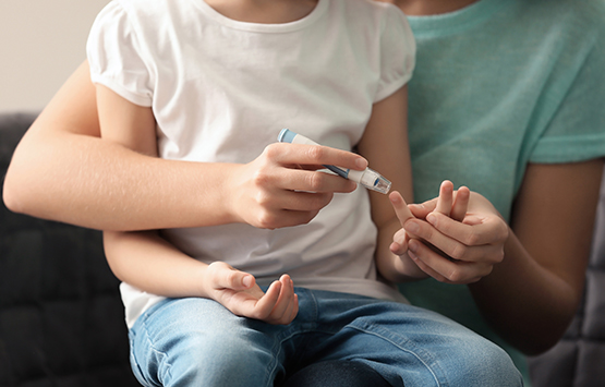 Mother holding her child and testing the child's blood suger levels with a finger prick tester